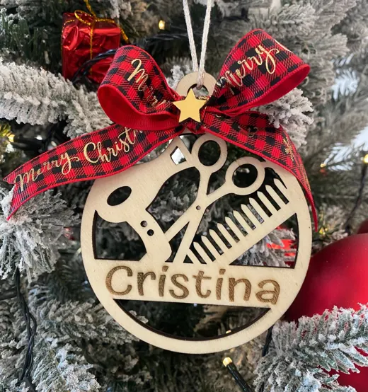 Pallina di Natale in legno con forbici e pettine traforati e il nome Cristina, sotto un fiocco rosso